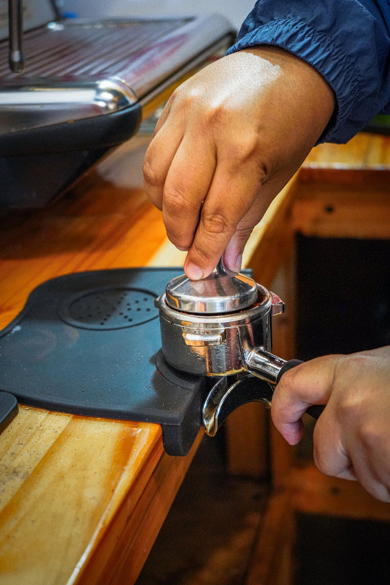 Person using a manual espresso grinder on a wooden counter.
